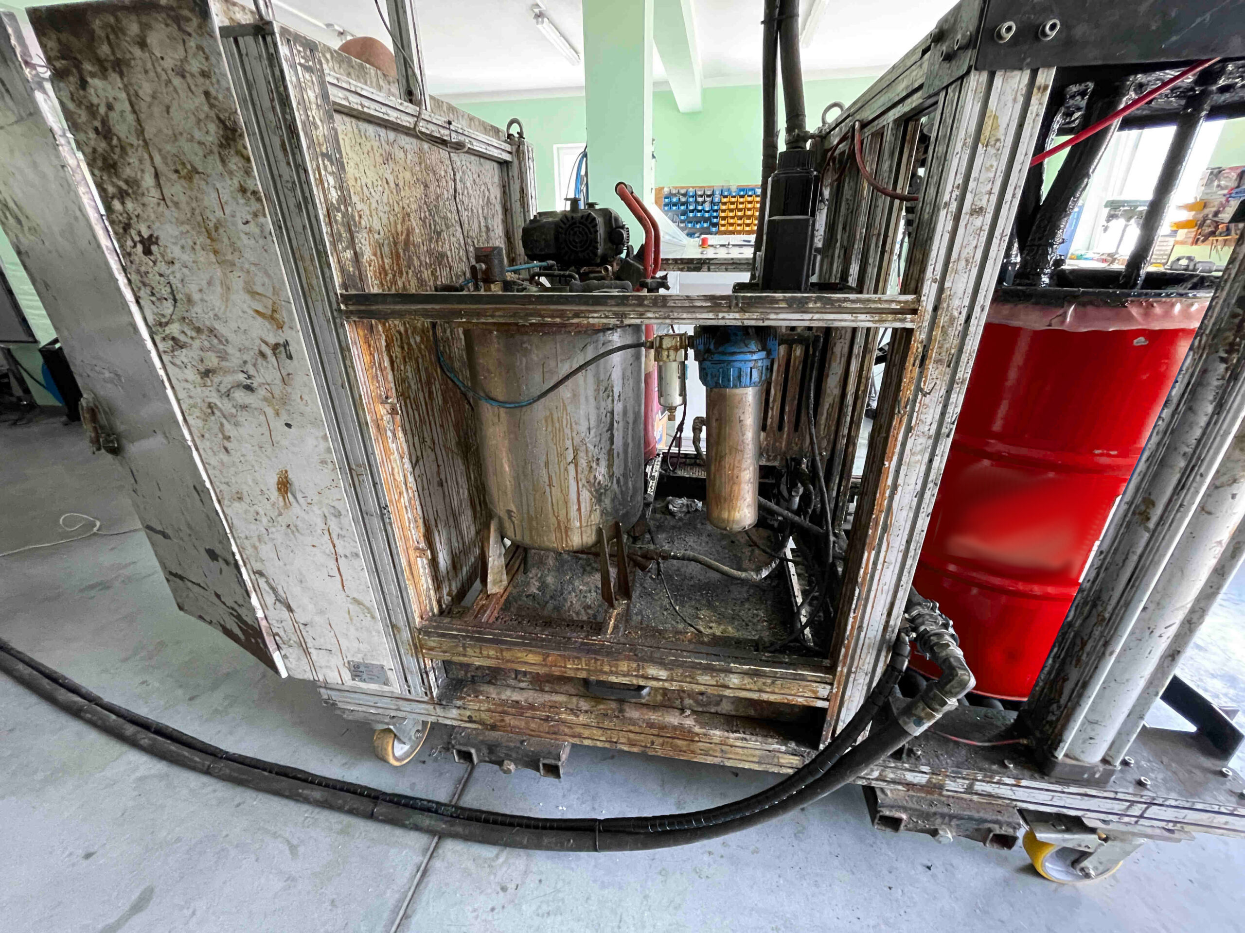 Zdjęcie maszyny heavyduty znajdującej się na hali serwisowej. Na zdjęciu widoczny jest przeznaczony do czyszczenia dozownik torowy. Po prawej stronie dozownika widoczna jest czerwona beczka z materiałem.